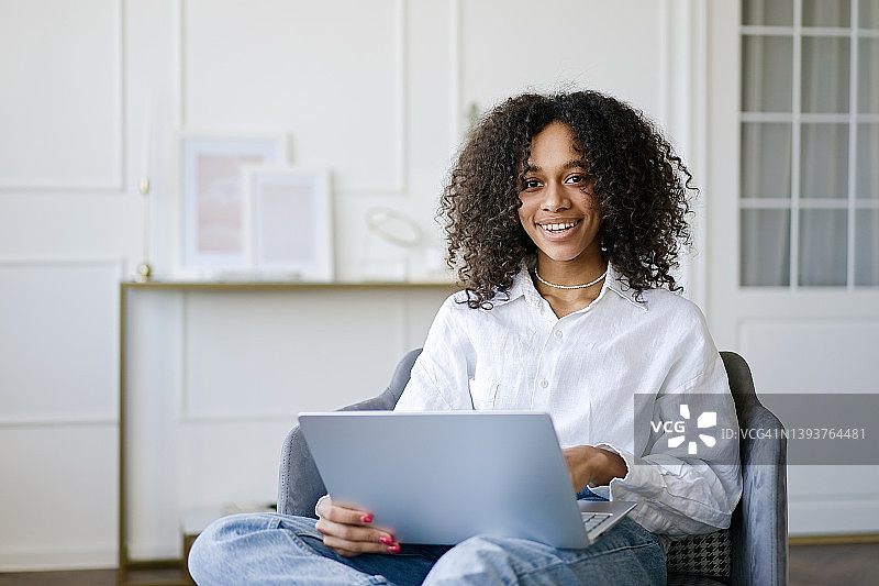 年轻的非洲裔美国女孩坐在客厅里用笔记本电脑工作图片素材