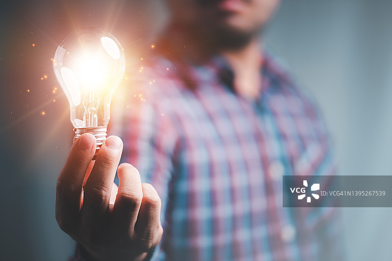 创意创新和灵感理念。男人的手拿着发光的灯泡，概念创意的灯泡闪闪发光。为企业可持续发展提供灵感。图片素材