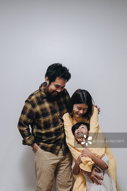 亚洲家庭幸福。父亲，母亲看着三岁的儿子，拥抱在一起。在白色背景上。图片素材