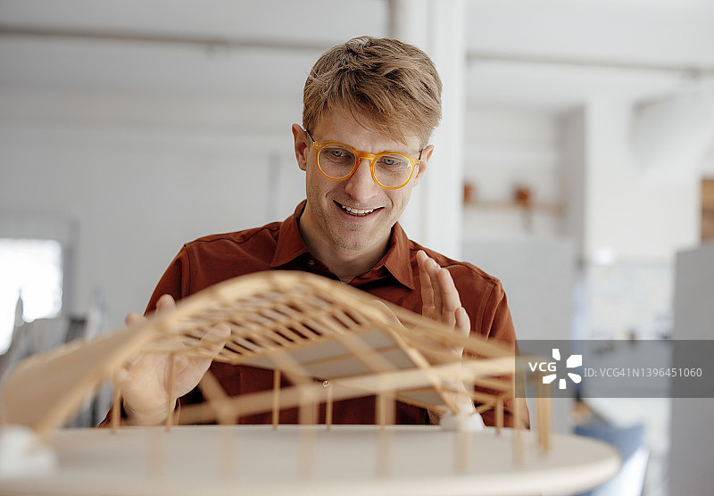 微笑的建筑师戴着眼镜看着办公室里的树叶形状的模型图片素材