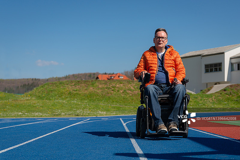 一个残疾人坐在电动轮椅上怀旧地坐在运动场上的蓝色跑步机上。图片素材