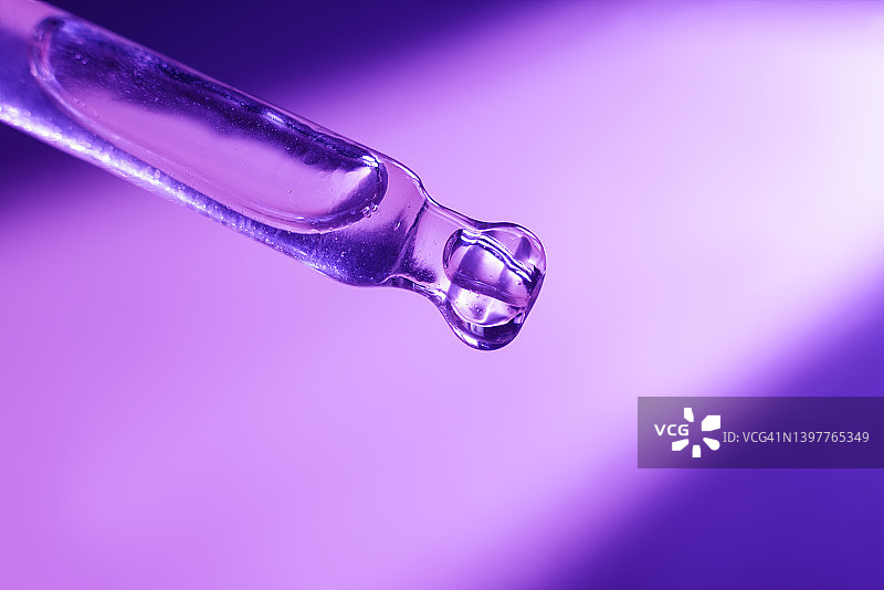 从化妆品玻璃滴管滴一滴透明质酸，天然血清在其末端的紫色背景。图片素材