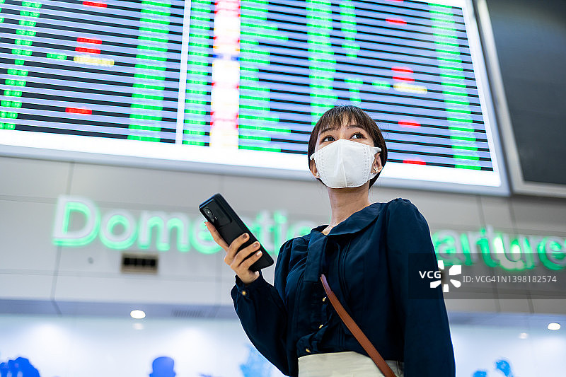 一名亚洲年轻女子在机场候机楼的航班时刻表前使用智能手机图片素材
