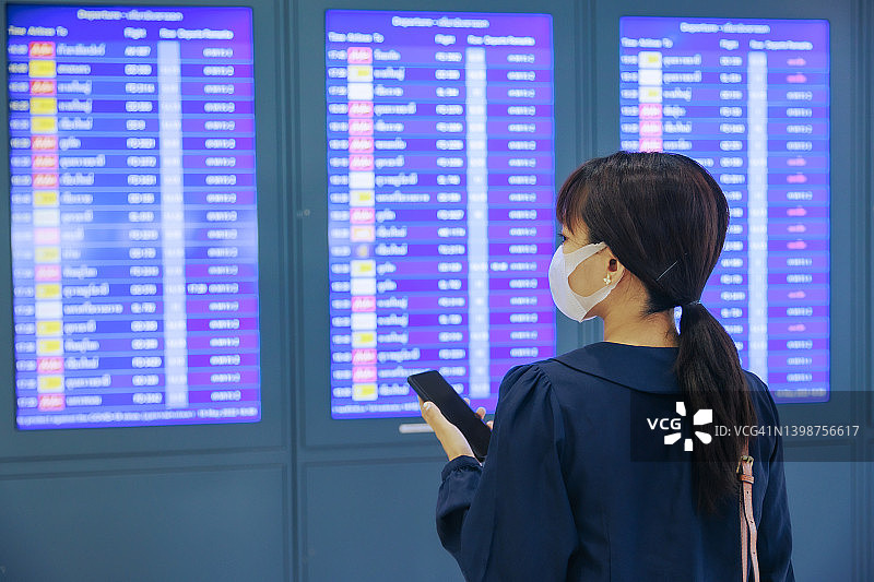 年轻的亚洲女商人戴着口罩在机场的登机牌上阅读。商务旅行的概念。图片素材