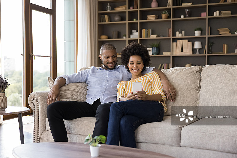 幸福的非洲夫妇坐在沙发上玩手机图片素材