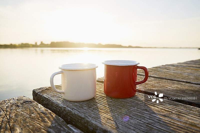 日落时分，在海边的码头上，两个搪瓷咖啡杯图片素材