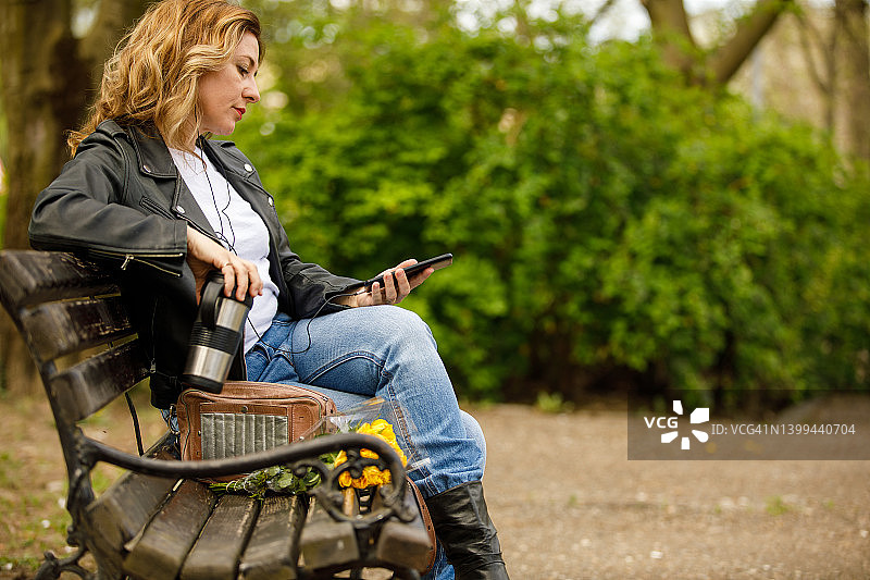 一边在公园喝咖啡，一边听音乐，一边用智能手机的金发女人的侧视图图片素材