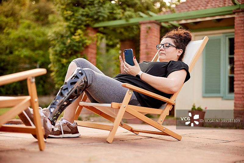 一个女人在躺椅上用智能手机放松。图片素材