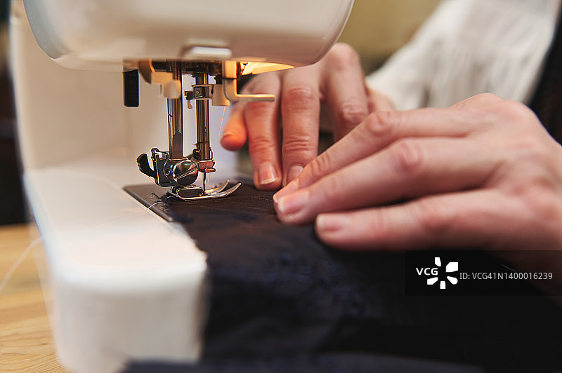 特写女时装设计师的手在缝纫机上缝制布料在裁缝工作室。时尚的设计理念图片素材