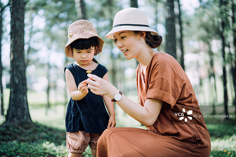 幸福的亚洲家庭享受大自然，母亲和小女儿在自然公园采摘鲜花。健康的家庭生活方式。亲情关爱。探索自然和户外乐趣图片素材