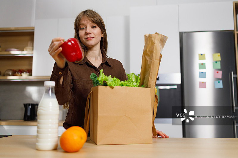 女人从纸袋里取出蔬菜和其他食物放到厨房的台面上图片素材