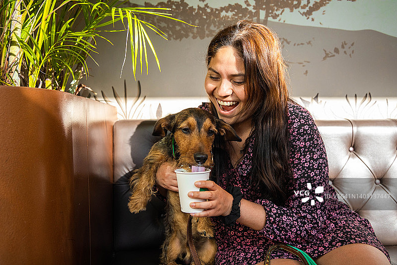 可爱的年轻腊肠狗在著名的咖啡馆喝着puppuccino，女人在笑。图片素材