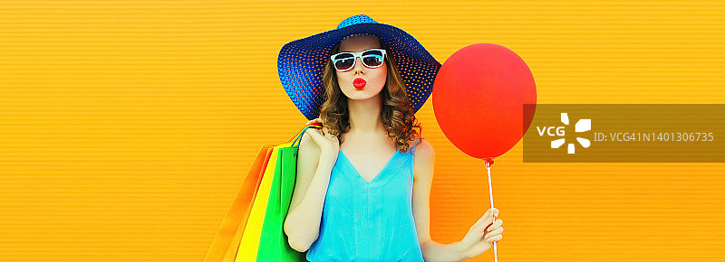 美丽快乐的年轻女子的肖像吹她的嘴唇与购物袋戴夏天的草帽在橙色的背景，空白的拷贝空间的广告文字图片素材