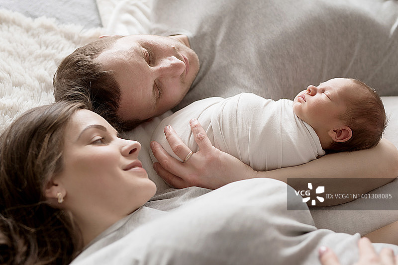 刚出生的婴儿在爸爸妈妈的怀里躺在床上。明信片母亲节和父亲节。儿童保护的一天。世界上幸福的一天。微笑的孩子。快乐的亲子关系图片素材
