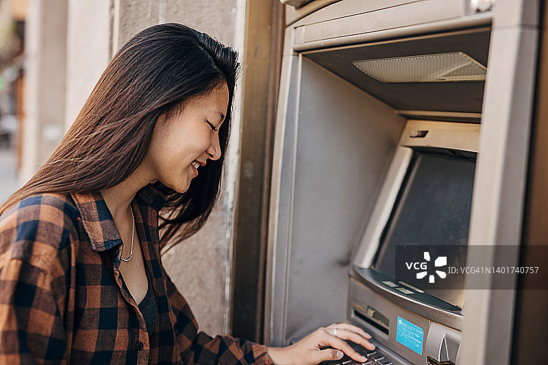 年轻的亚洲女性使用信用卡在自动提款机取钱图片素材