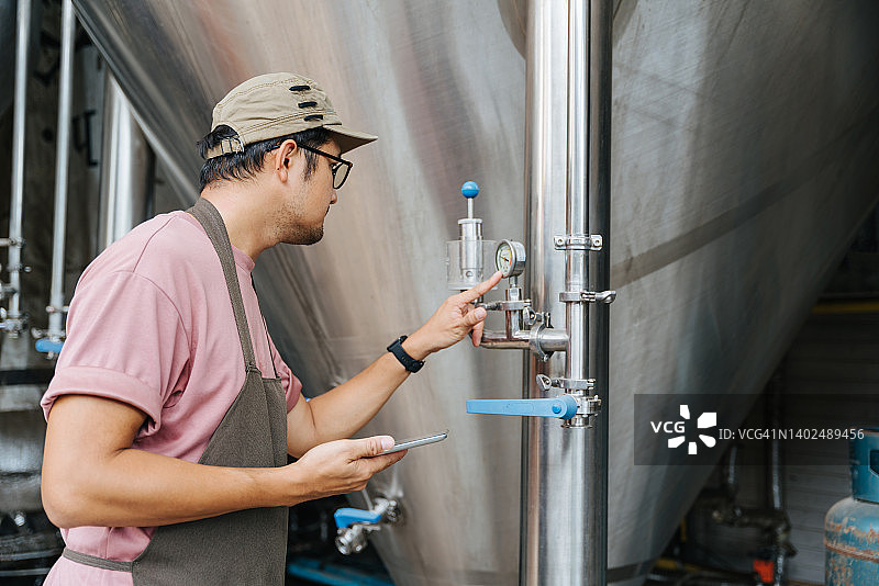 在仓库的精酿啤酒厂，一名酿酒师正在检查压力表。图片素材