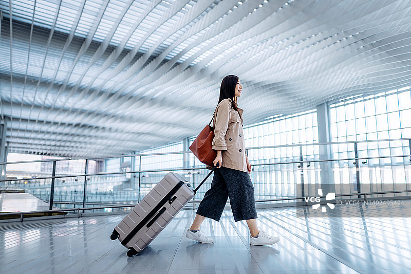 年轻的亚洲女性提着行李箱走在机场候机楼的侧面。准备旅行。旅行和度假的概念。出差的商务人士图片素材