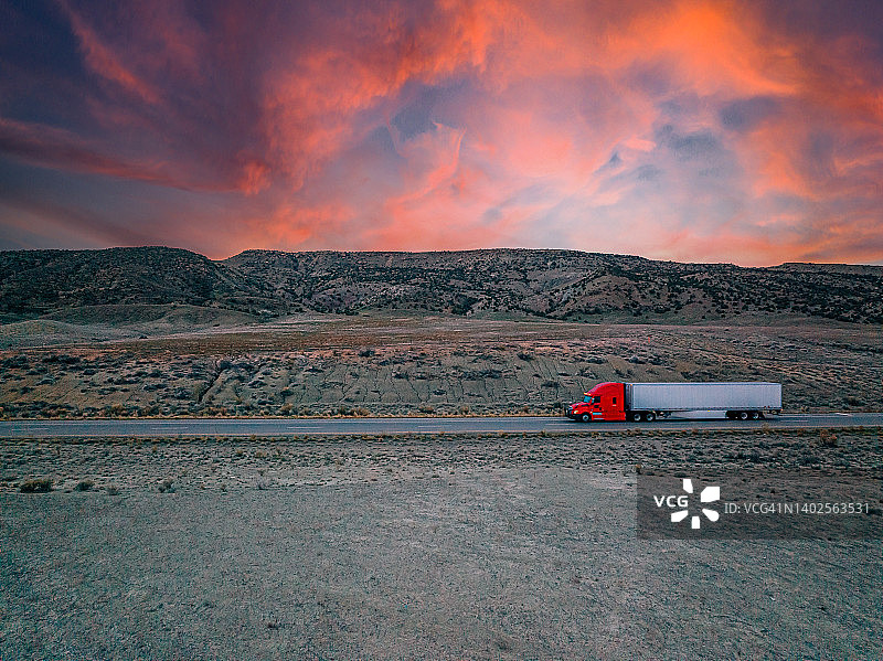 无人机拍摄的红色半挂车在高速公路上与彩色的日落图片素材