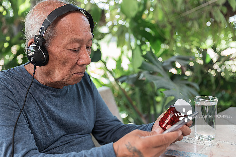 老年男子在家里用智能手机与医生进行远程医疗通话，亚洲老年69岁图片素材