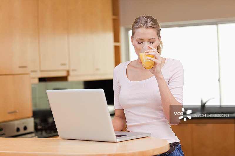 女人一边喝橙汁一边用笔记本图片素材