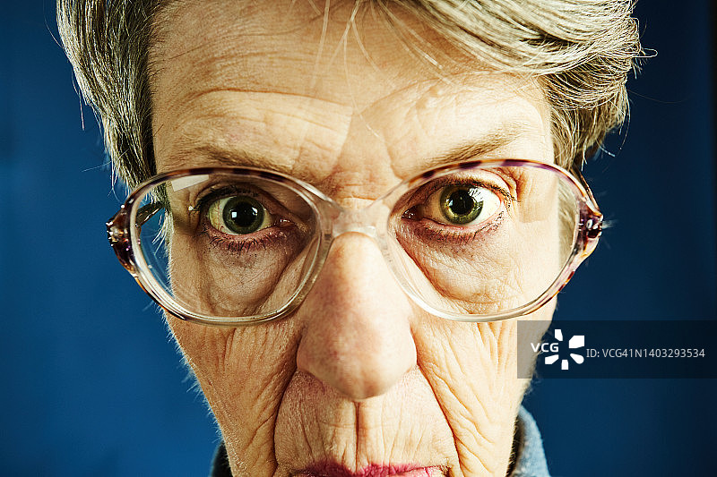 一位老妇人通过广角镜头扭曲的眼镜茫然地盯着相机图片素材