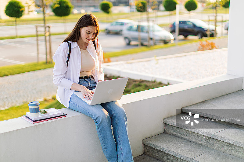 一位女学生正在大学楼前使用笔记本电脑图片素材