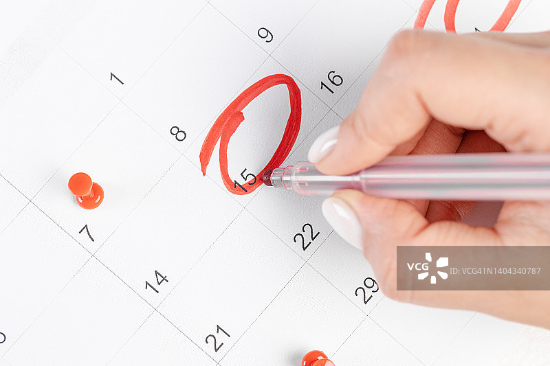近距离观察员工女性手用红笔在日历2022上写时间表，以预约会议或管理时间表，每天在家工作的概念图片素材