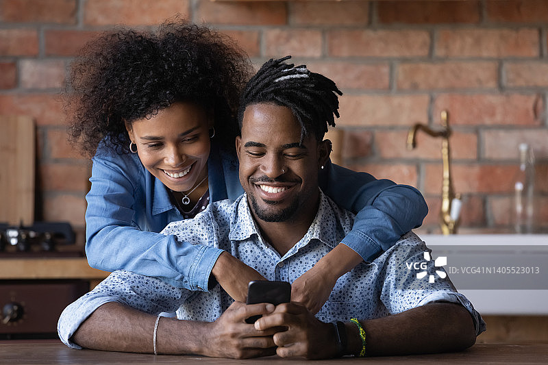 幸福的混血夫妇在家使用智能手机应用程序。图片素材