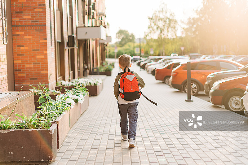回到学校。可爱的孩子背着双肩包去上学。小男孩背着书包。小学生去上课。孩子放学后在街上散步。后视图。图片素材