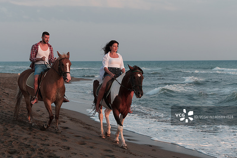 一对可爱的年轻夫妇穿着夏天的衣服，在夕阳下的沙滩上骑马。背景是大海和日落。有选择性的重点图片素材
