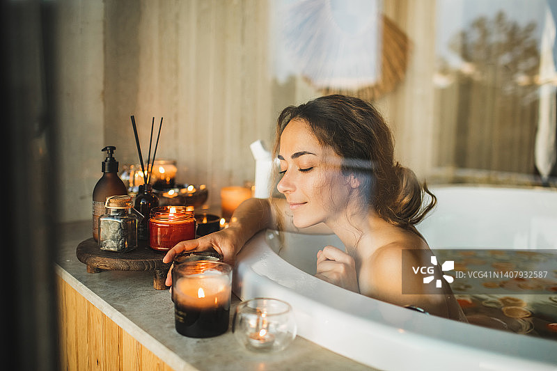 美丽的年轻女子在极可意浴缸里放松，有柑橘柑橘和柠檬，还有蜡烛。图片素材