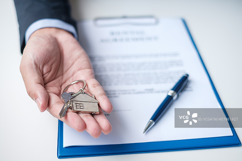 男子持有家里的钥匙在签署家里的合同文件。合同协议、房地产、买卖和保险概念图片素材