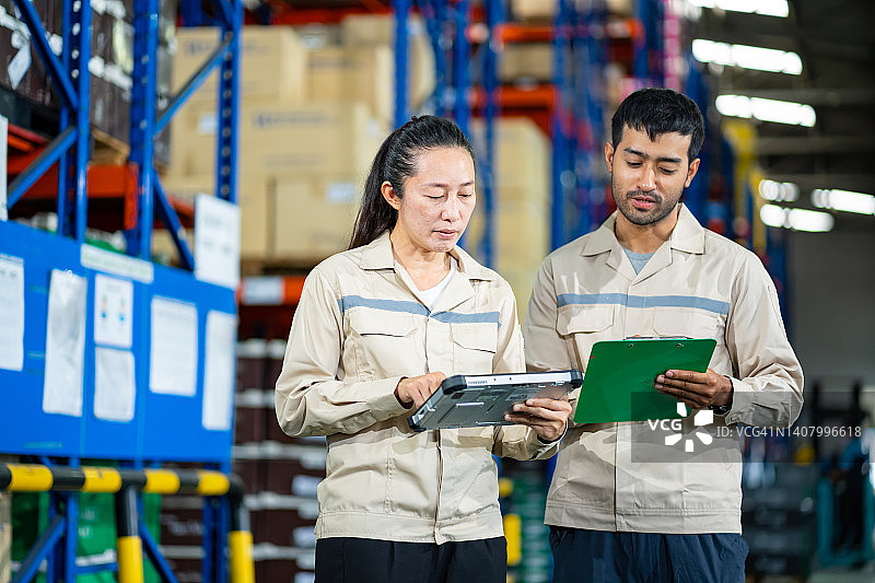 亚洲经理和亚洲员工走进仓库检查产品入库情况，并使用数字平板电脑对仓库托盘产品进行盘点。图片素材