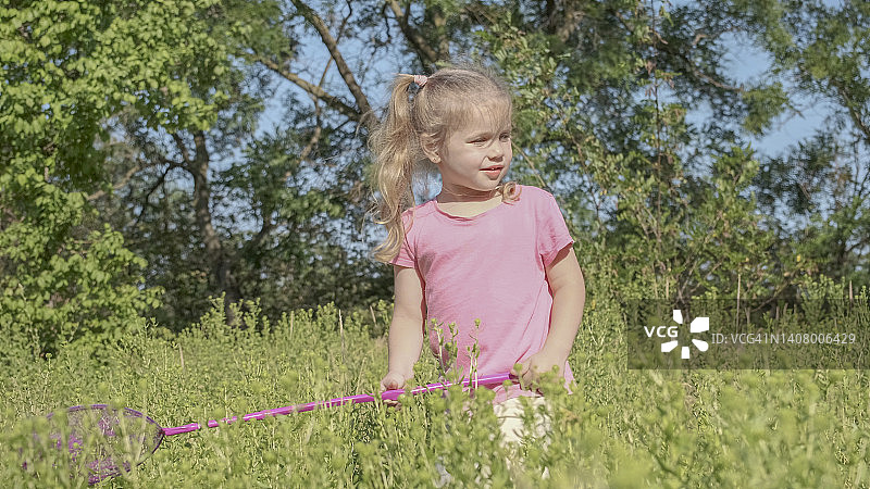 小女孩在城市公园玩高草的蝴蝶网。阳光灿烂的日子，可爱的小女孩在草地上玩空中捕虫网。图片素材