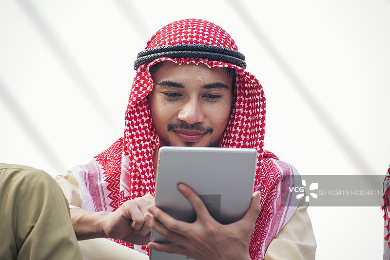 伊斯兰男子使用智能手机应用程序组织日程安排重点手握智能手机穆斯林现代阿联酋城市。阿拉伯男子穿着头巾和穆斯林正装在网上发送短信的生活方式图片素材