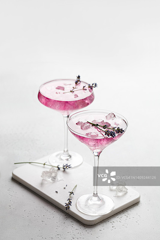 紫色薰衣草鸡尾酒饮料在一个白色的板和白色的背景与冰和薰衣草花。
冰凉的夏日饮品，柠檬水。图片素材