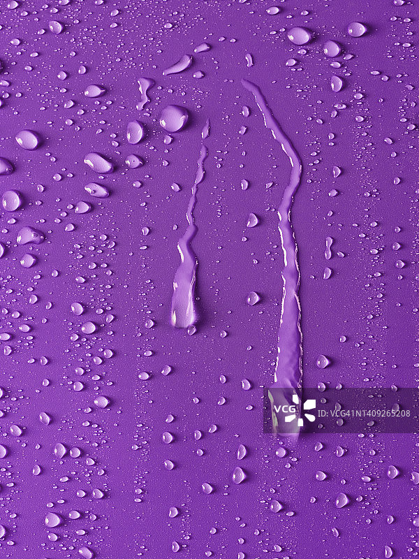 雨滴在紫色的背景上滑动。图片素材