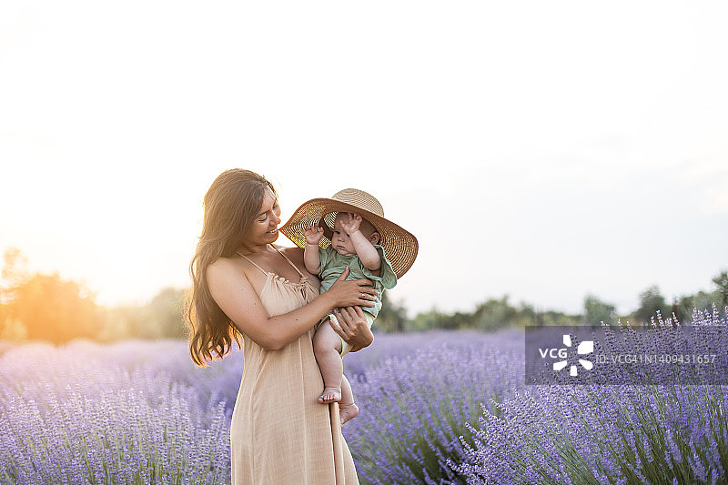 年轻的女人和她的女儿在夏天的裙子和太阳帽散步和拥抱在薰衣草田在日落图片素材