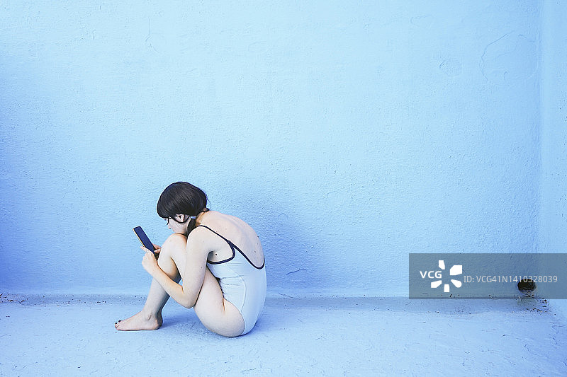 一名女子在游泳池的蓝色墙壁前使用手机图片素材