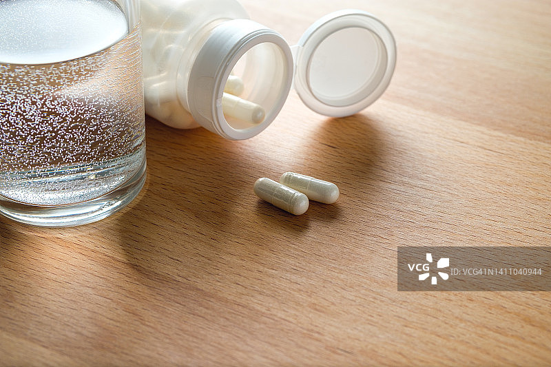 厨房的木桌上放着药片和一杯水。服用维生素、止痛药、药物和膳食补充剂。预防和治疗疾病、保健和医药的概念。计划和准备怀孕。图片素材