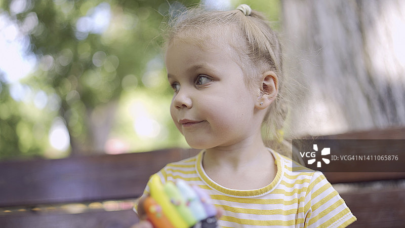 小女孩拿着五颜六色的姜饼。特写的可爱的小女孩坐在公园的长凳上，看着周围的饼干。图片素材