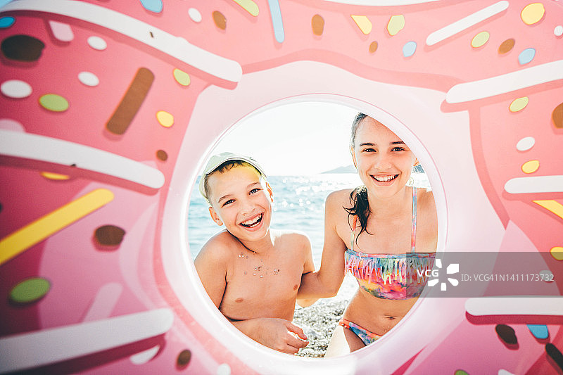 哥哥和妹妹在海滩上享受夏天。可爱的孩子们拿着粉色的戒指在沙滩上玩耍。图片素材