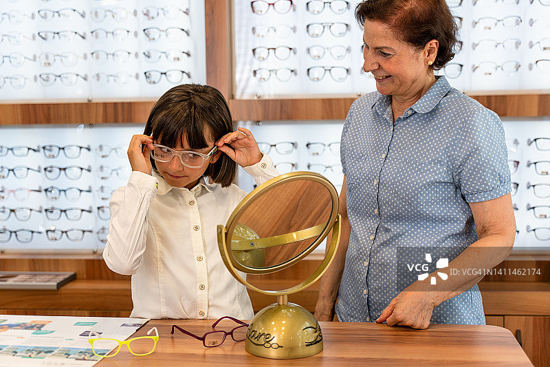 微笑的女孩顾客在眼镜店挑选眼镜图片素材