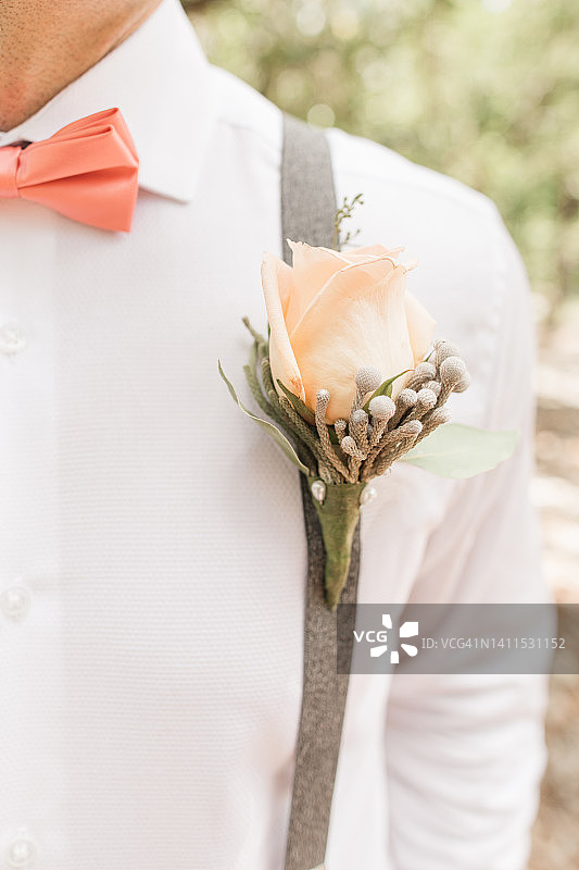 新郎的粉色领结和玫瑰Boutonnière在白色纽扣衬衫与背带裤搭配在婚礼上7月在户外棕榈滩，佛罗里达州图片素材