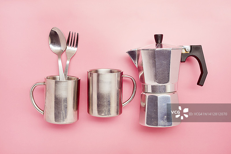 静物的马克杯，餐具和炉顶咖啡壶在粉红色的背景图片素材