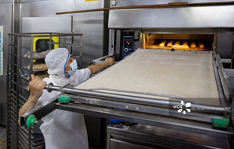一名男子在面包店工作，从烤箱中取出面包图片素材