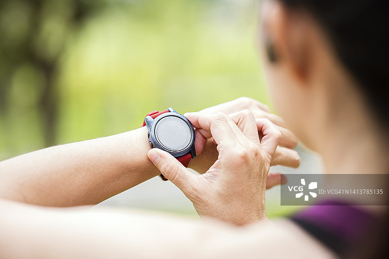 健康护理技术中的即时心率监测器和脉搏检查器。在一个城市公园里，一位亚洲女运动员在户外运动后休息，用她的智能手表测量心率和脉搏。图片素材