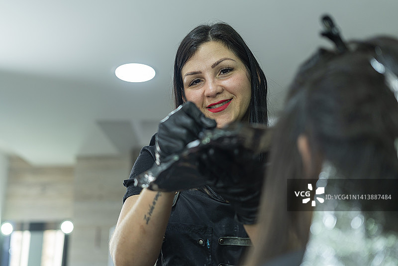 一位美发沙龙的女老板一边给她的客户染头发，一边看着塑造她的相机图片素材