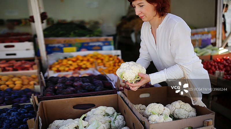 市场上的中年妇女用生态网袋选择菜花图片素材