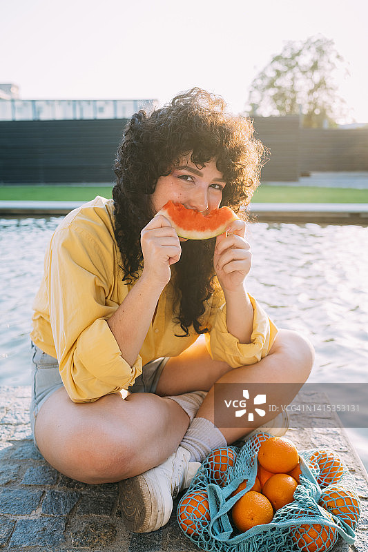 用网袋装橘子的女人在池塘边吃西瓜图片素材